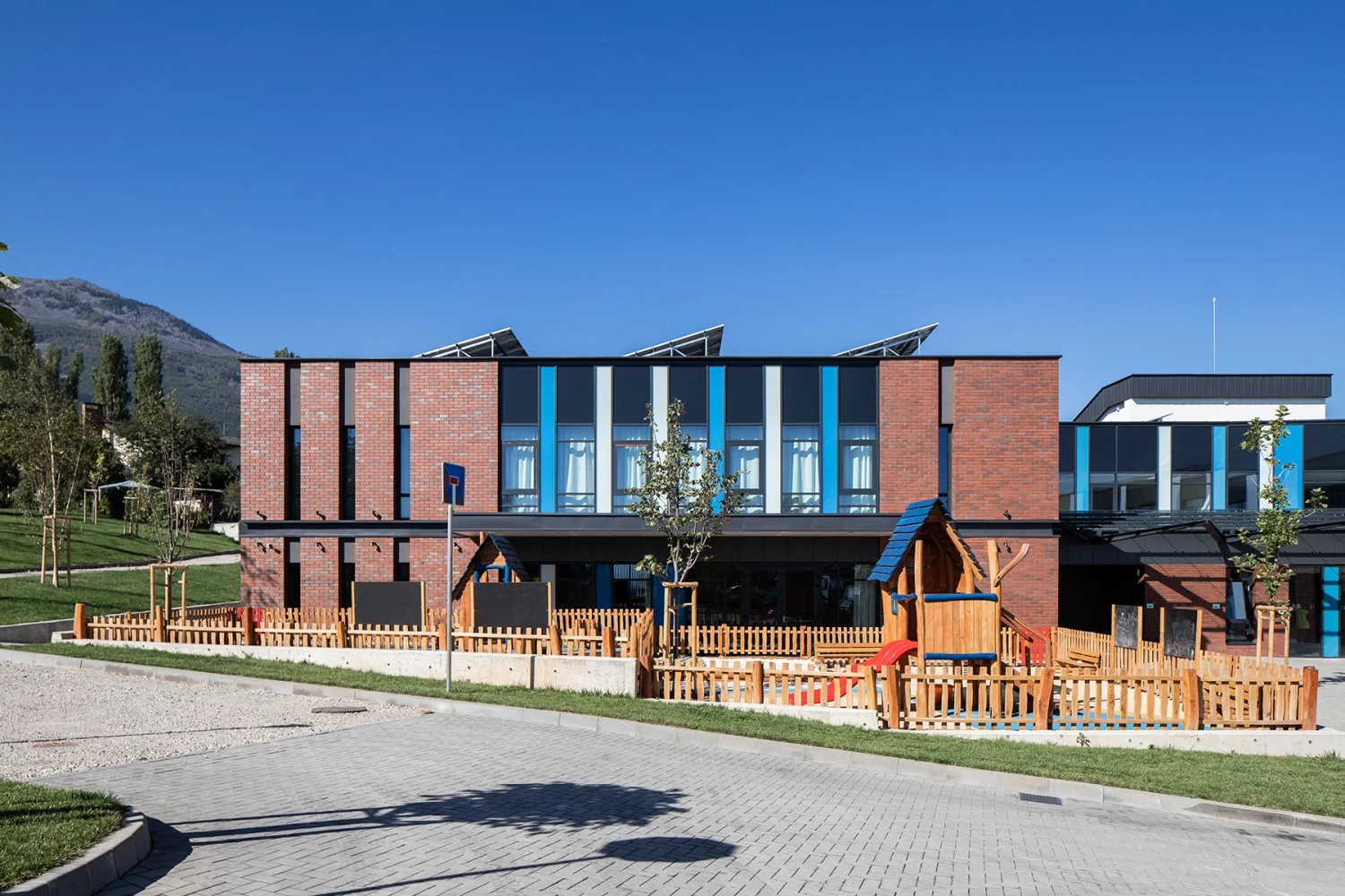 Фасада на BRITANICA Park School с тухлена облицовка, големи остъклявания и зона за игра