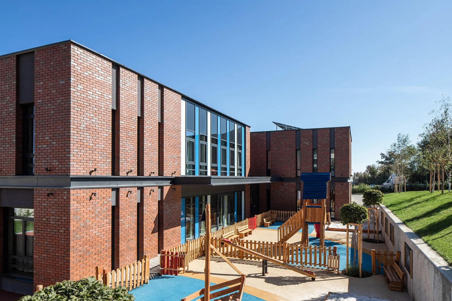 Странична фасада на BRITANICA Park School с тухлени обеми, остъкляване и детска площадка
