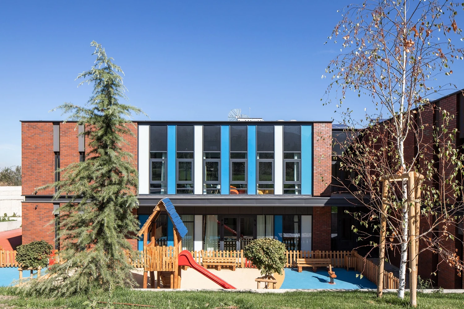 Главна фасада на BRITANICA Park School със сини рамки на прозорците и външна зона за игра