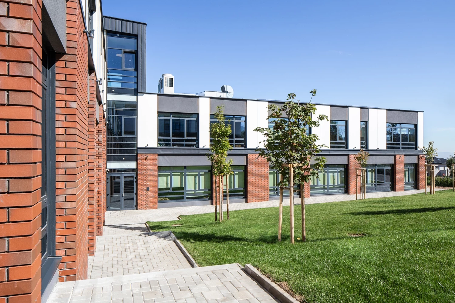 BRITANICA Park School с тухлени и бели фасадни елементи към озеленено дворно пространство