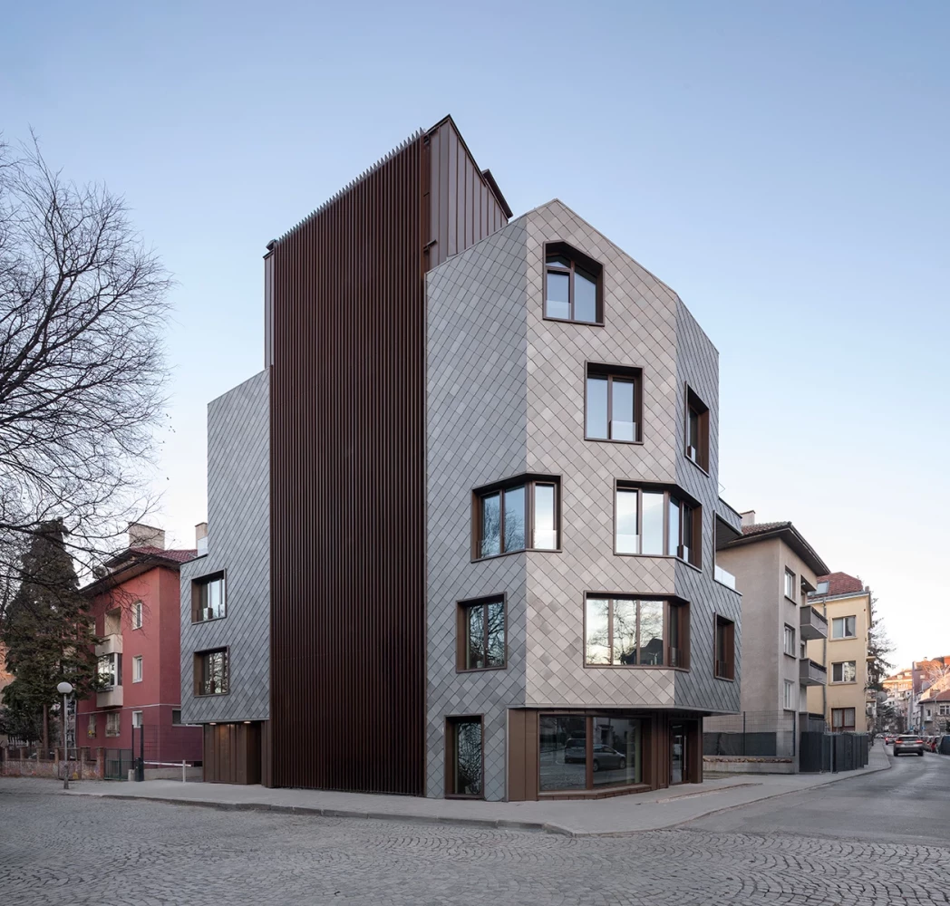 Corner view of KA11 with a titanium-zinc facade and dark vertical cladding