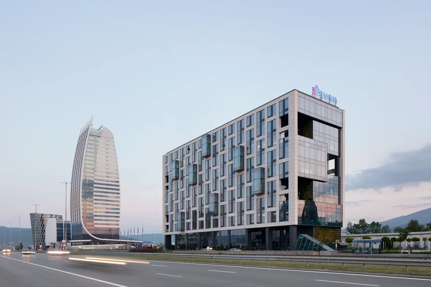 Ъглов изглед към Space Tower с дълга остъклена фасада и висока сграда на заден план
