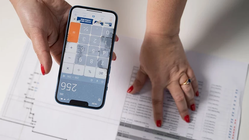 Calculator on a smartphone over a printed project schedule and table